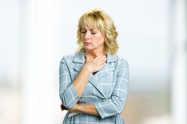 Portrait of worried mature woman. Adult lady holding hand on neck and close eyes, painful feelings.