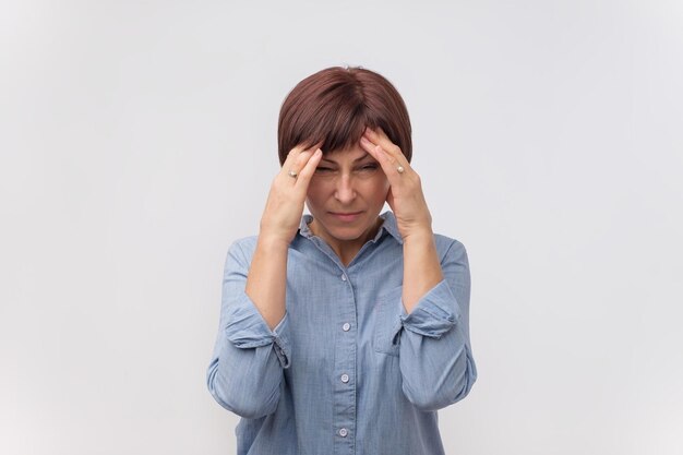 Ritratto di donna matura preoccupata che tocca le sue tempie sentendo lo stress