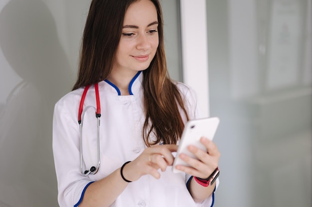 Portrait of youg female doctor using phone during break in clicic