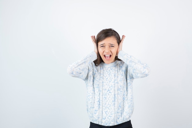 Portrait of young adorable girl in sweater covering her ears.