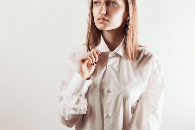 Portrait of young adult woman holding collar of white shirt with her hand, 