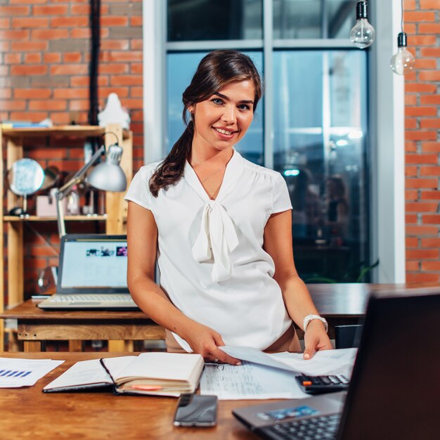 Portrait of young advertising agent holding papers standing at her workplace.