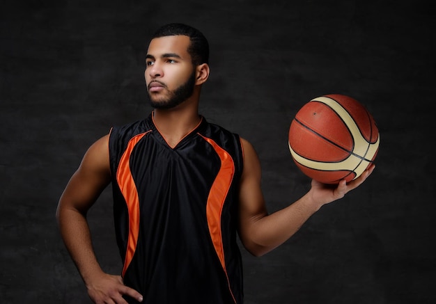 Portrait of a young African-American basketball player in sportswear isolated over dark background.