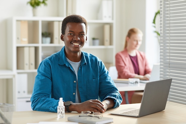 Portrait of young African-American man smiling working at desk in office with colleagues