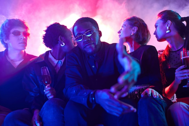 Portrait of young african american man with diverse group of\
friends at party in neon lights