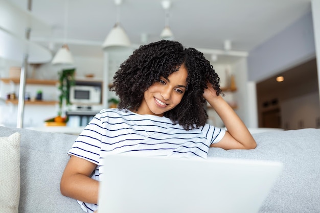 Photo portrait of young african american woman using laptop and smiling while sitting on sofa at home copy space