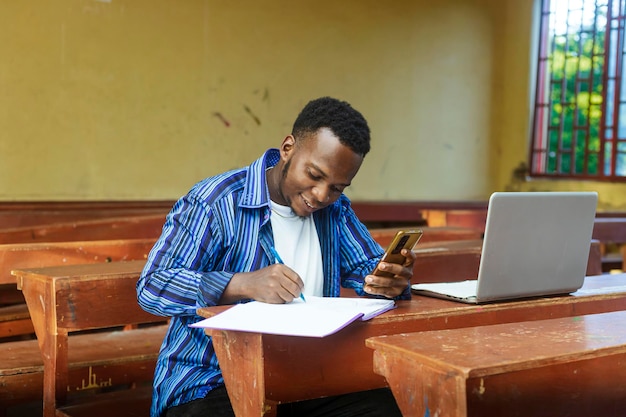 Portrait of a young african boy using a mobile phone while doing his homework