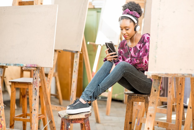그림을 그리기 위해 스튜디오에서 휴식 시간에 전화를 들고 앉아 있는 젊은 아프리카 민족 학생의 초상화