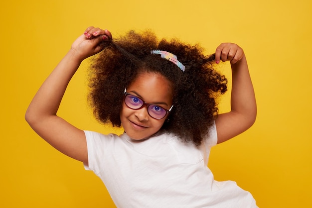 Portrait of a young african girl in glasses smiling and rejoicing on a clean yellow background