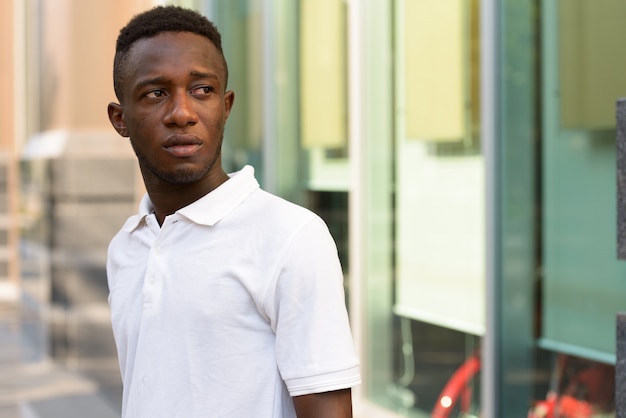 Portrait of young African man thinking and looking back in the city outdoors