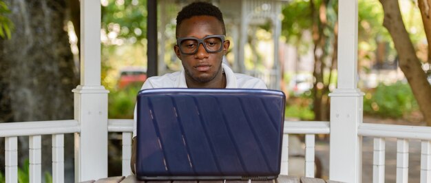 Ritratto di giovane uomo nerd africano come studente con gli occhiali al parco all'aperto