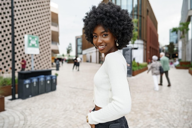 Photo portrait of young african woman with afro hairstyle smiling in urban background