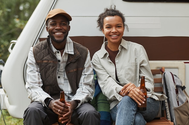 Portrait of young africanamerican couple relaxing outdoors while camping with trailer van and lookin...