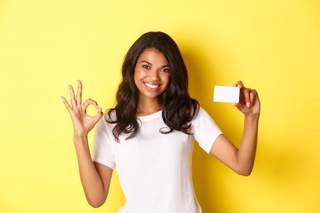 Portrait of young africanamerican girl showing credit card making okay sign and smiling recommending...