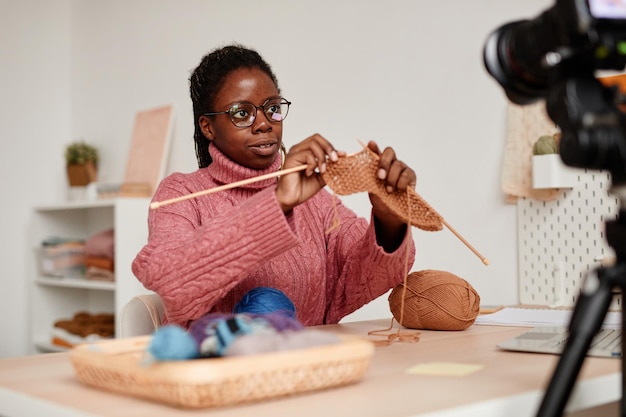 Portrait of young africanamerican woman knitting at home and recording video or online education class