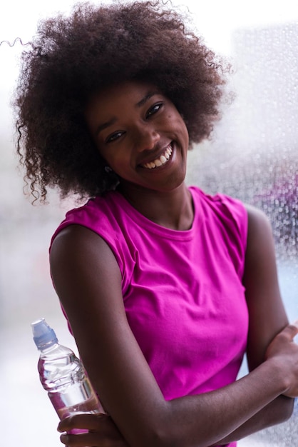 Photo portrait of young afro american woman in gym on work out break while teaking breath and fresh water rainy day and bad weather outdooor