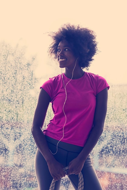 portrait of young afro american woman in gym on workout break while listening music on earphone  and dancing  rainy day and bad weather outdooor