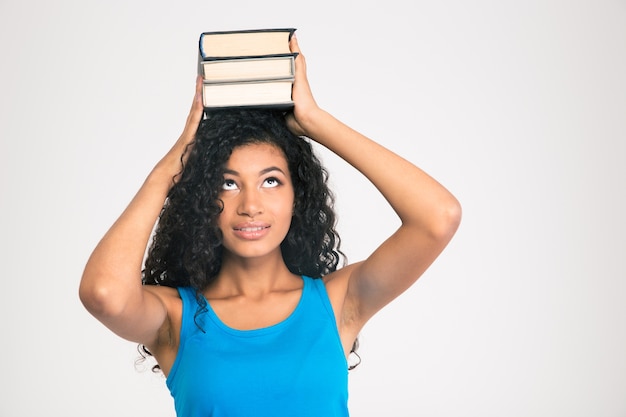 Photo portrait of a young afro american woman holding books on the head and looking up isolated on a white wall