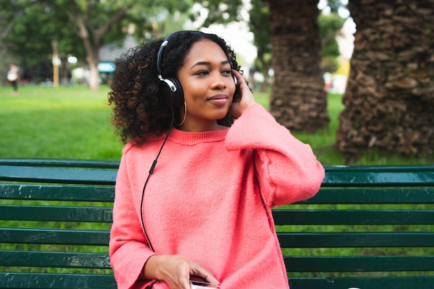 Ritratto di giovane donna afroamericana che ascolta la musica con le cuffie e il telefono cellulare nel parco.