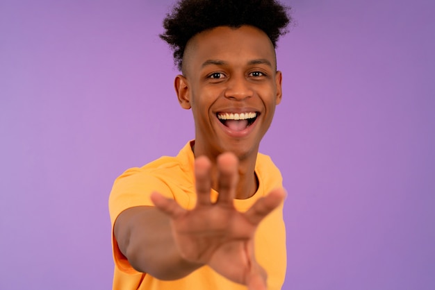 Photo portrait of a young afro man smiling and trying to catch something with his hand while standing against isolated background.