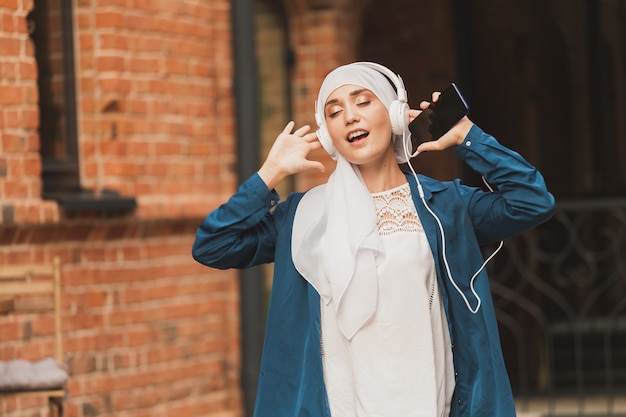 Portrait of young arabian muslim woman listening music with headphone and dancing. Feminism, woman independence and leisure concept.