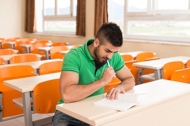 혼자 교실에 앉아 책을 가진 젊은 아랍 남자 대학생의 초상화