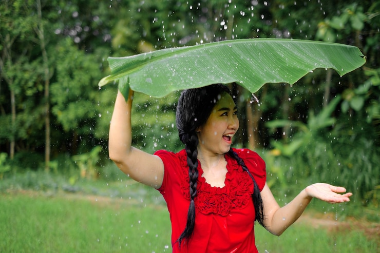 Photo portrait of a young asia woman was under a banana leaf taking shelter from the rain in the green garden background