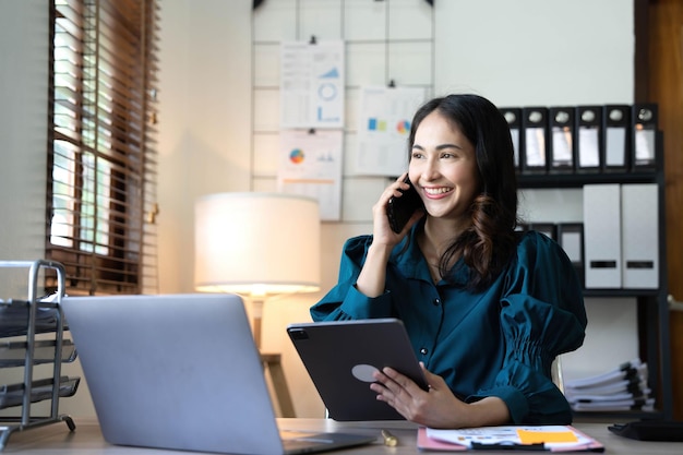 Portrait of young asian business woman talk on smartphone write notebook laptop in home office Beautiful girl at desk computer take home order Startup business asia woman online sme telemarketing