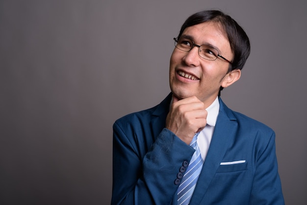 Portrait of young Asian businessman against gray wall