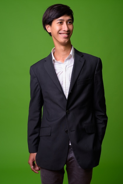 Portrait of young Asian businessman against green wall