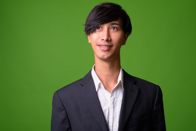 Portrait of young Asian businessman against green wall