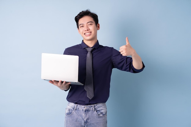 Portrait of young Asian businessman using laptop on blue background