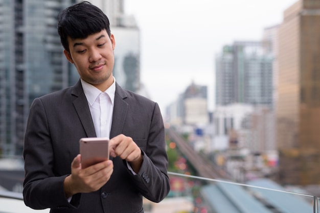 街の景色に対して電話を使用して若いアジアのビジネスマンの肖像画