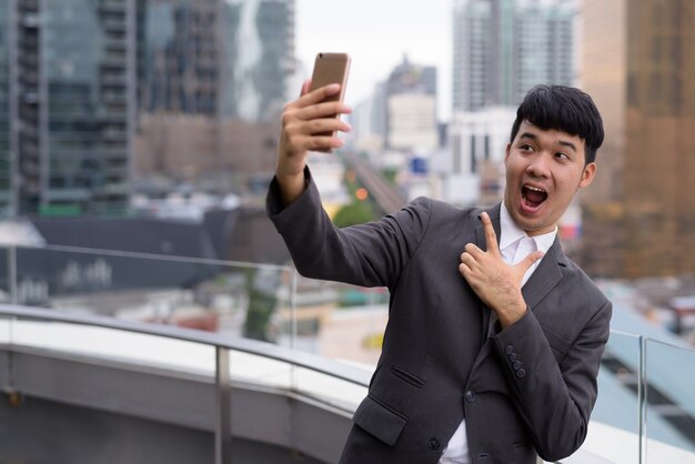 Portrait of young Asian businessman using phone against view of the city