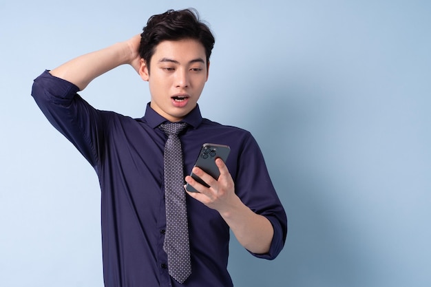 Portrait of young Asian businessman using smartphone on blue background
