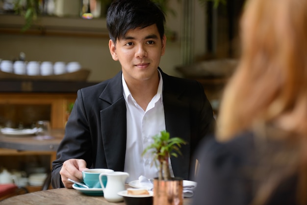 Portrait of young Asian businessman and young Asian businesswoman together relaxing at the coffee shop