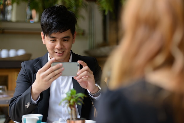 Portrait of young Asian businessman and young Asian businesswoman together relaxing at the coffee shop