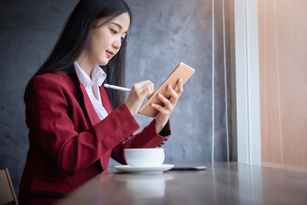 Portrait of Young asian businesswoman sitting indoors in cafe using digital tablet with coffee. Business success concept.