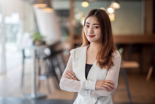 사무실에 서있는 젊은 아시아 사업가의 초상화입니다. 카메라 좀 봐.