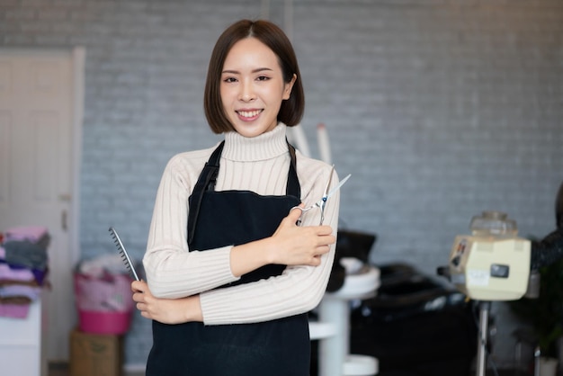 資格のあるヘアカット ツールを保持している若いアジア女性美容師の肖像画