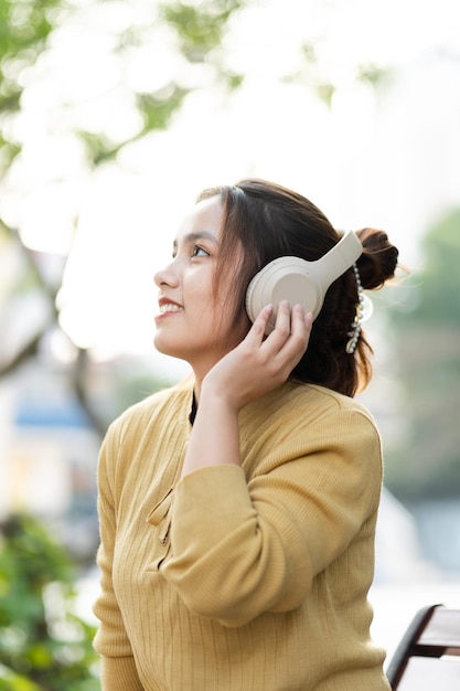 Портрет молодой азиатской девушки, слушающей музыку в парке