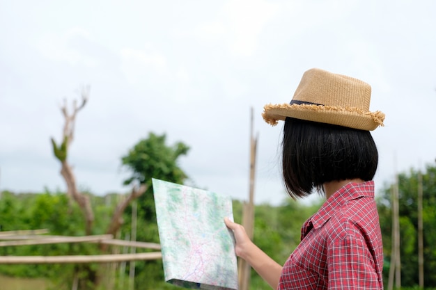 屋外の自然の背景に立っている間マップを保持している若いアジアの女の子旅行者の肖像画