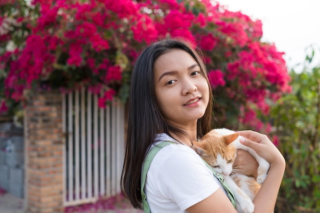 猫の屋外の美しい花の背景を持つ肖像画若いアジアの女の子