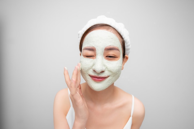 Photo portrait of young asian girl with clay mask over white background.