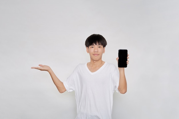 Portrait young Asian handsome cheerful guy wears in a white t-shirt  showing a blank smartphone screen and pointing with palm