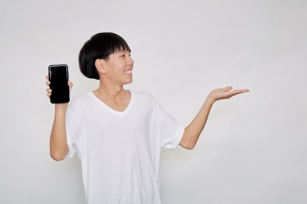 Portrait young Asian handsome cheerful guy wears in a white t-shirt  showing a blank smartphone screen and pointing with palm