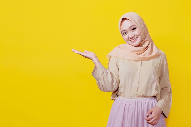 Foto ritratto di una giovane donna asiatica che sorride con un'espressione allegra, mostra qualcosa di straordinario in un panno casual sul muro giallo