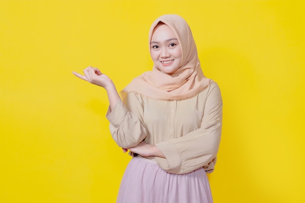 Photo portrait of young asian lady smiling with cheerful expression, shows something amazing in casual cloth over yellow wall