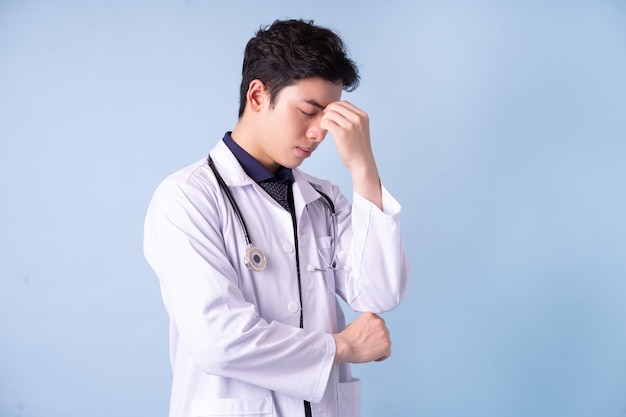 Portrait of young Asian male doctor on blue background