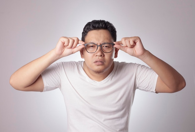 Portrait of young Asian man adjusting eyeglasses checking his sight problem over white background